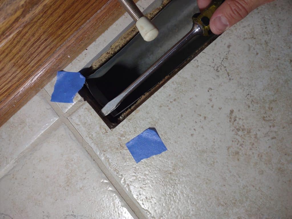 Before repairing bathroom tile, it's important to figure out the underlying issue. Using a screwdriver to probe beneath a loose tile with cracked grout.