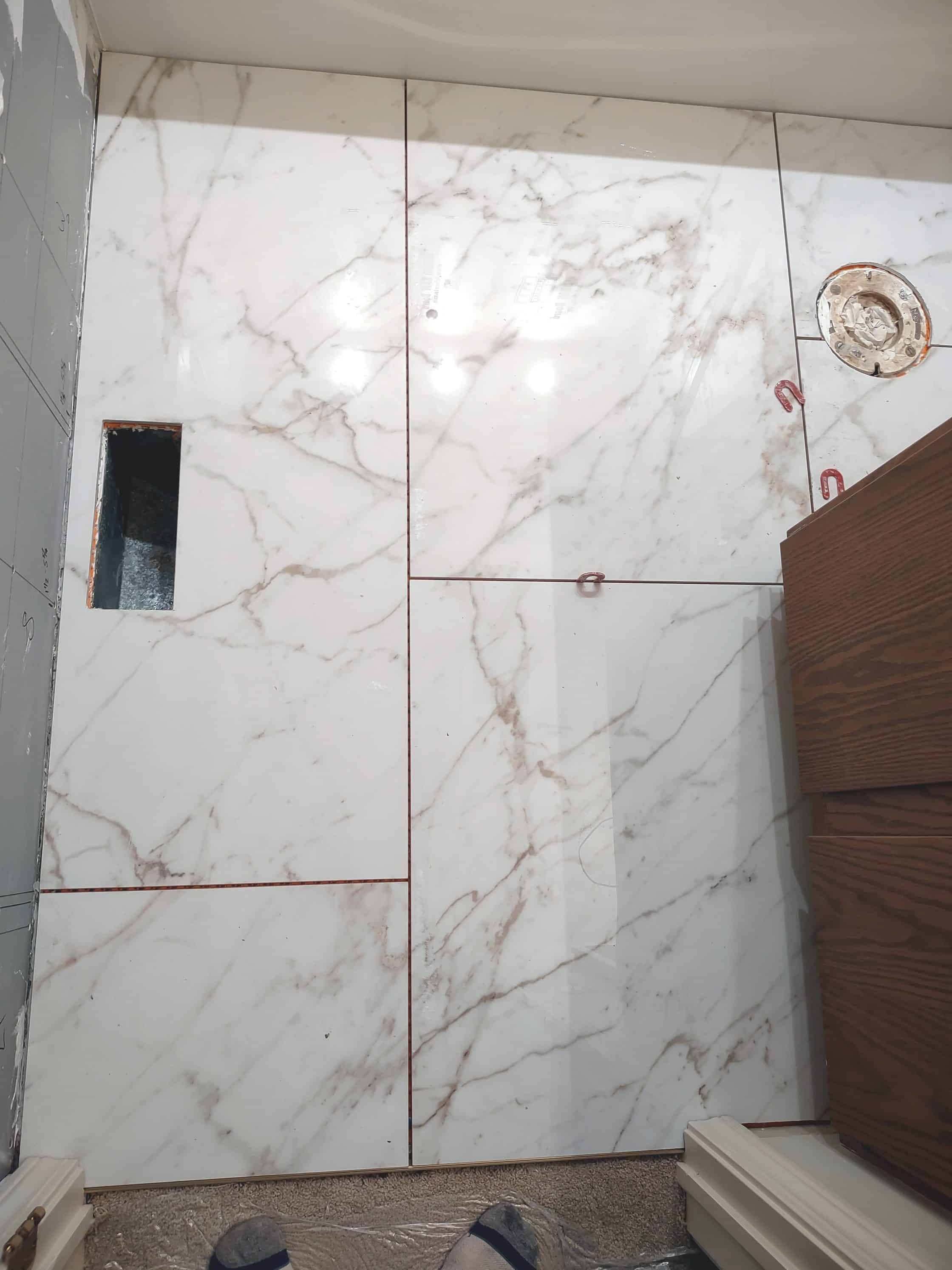 Large-format marble-look porcelain tiles installed on a small-bathroom floor.